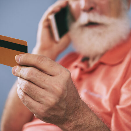 Elderly buyer holding credit card in his hand while placing a phone order